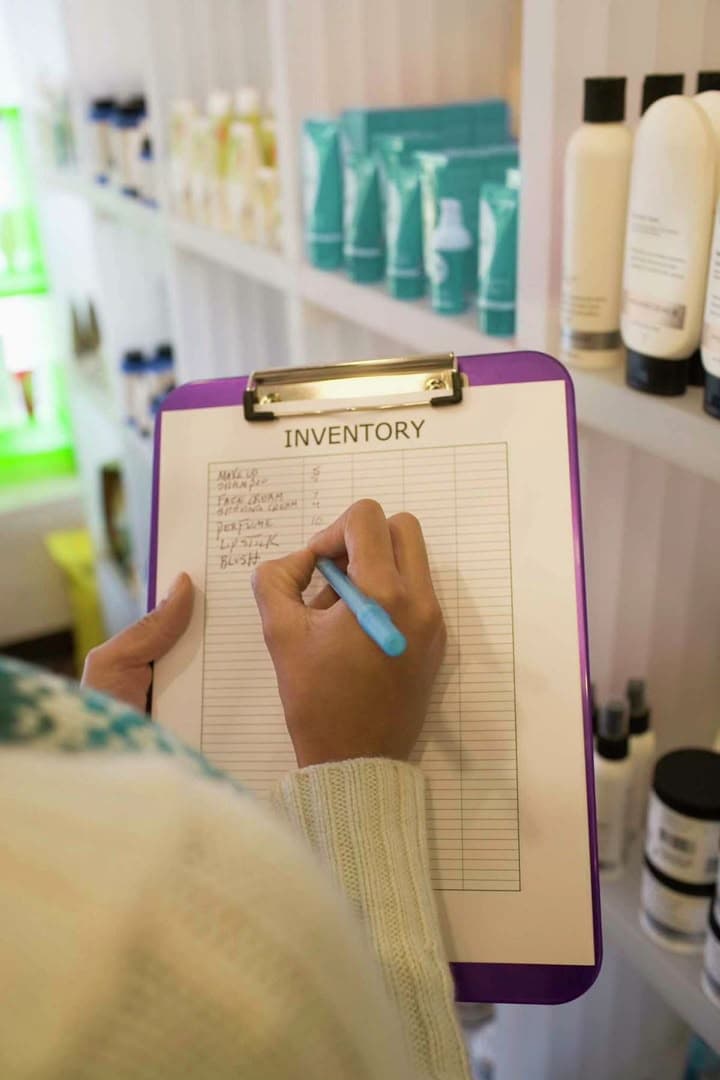 Store staff writing stock counts on a paper inventory clipboard between shelves